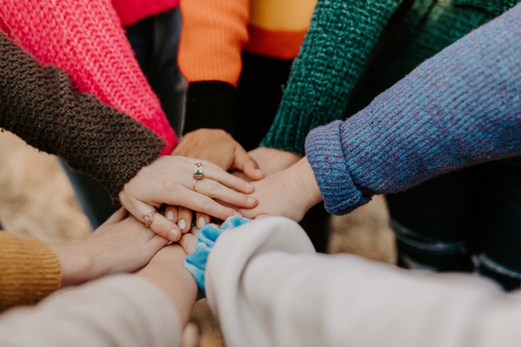 Hands stacked in unity, diverse sweaters symbolize teamwork.