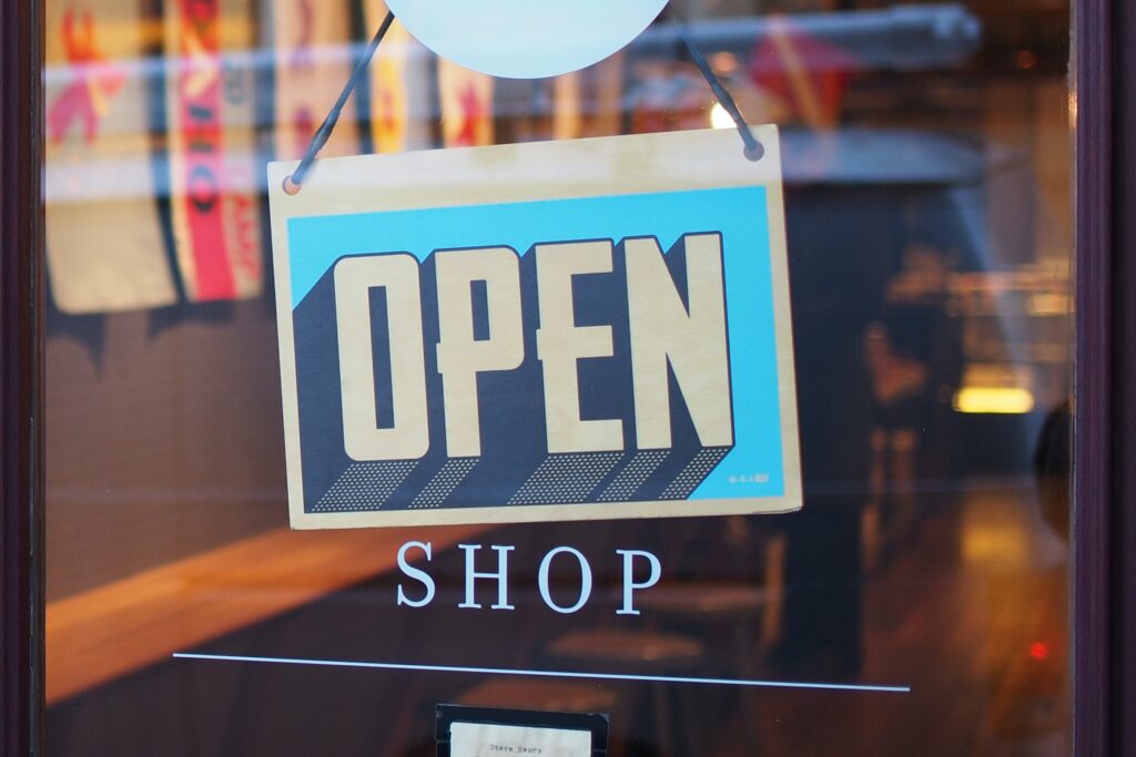 A clear 'OPEN SHOP' sign in bold lettering displayed on a glass door, indicating the business is ready to welcome customers.